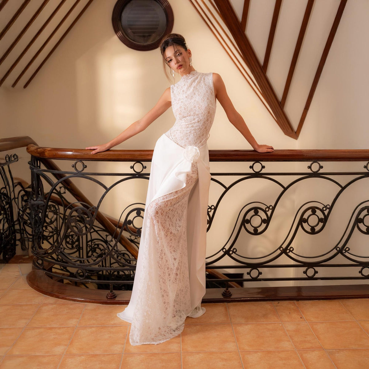 May include: A sleeveless white gown with a high neckline and a flowing skirt. The bodice is adorned with delicate lace, and the skirt features a layered design with a lace underlay. A floral accent adorns the waist, adding a touch of elegance.