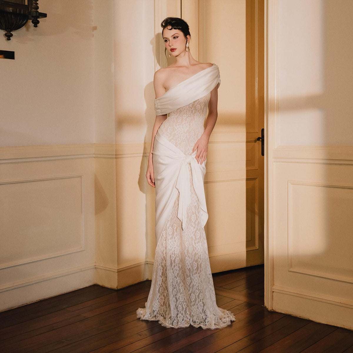 May include: A floor-length off-the-shoulder gown featuring a white satin bodice drape and a fitted lace skirt. The dress includes a gathered satin fabric detail at the waist that creates a side knot effect, transitioning into a full-length lace hem.