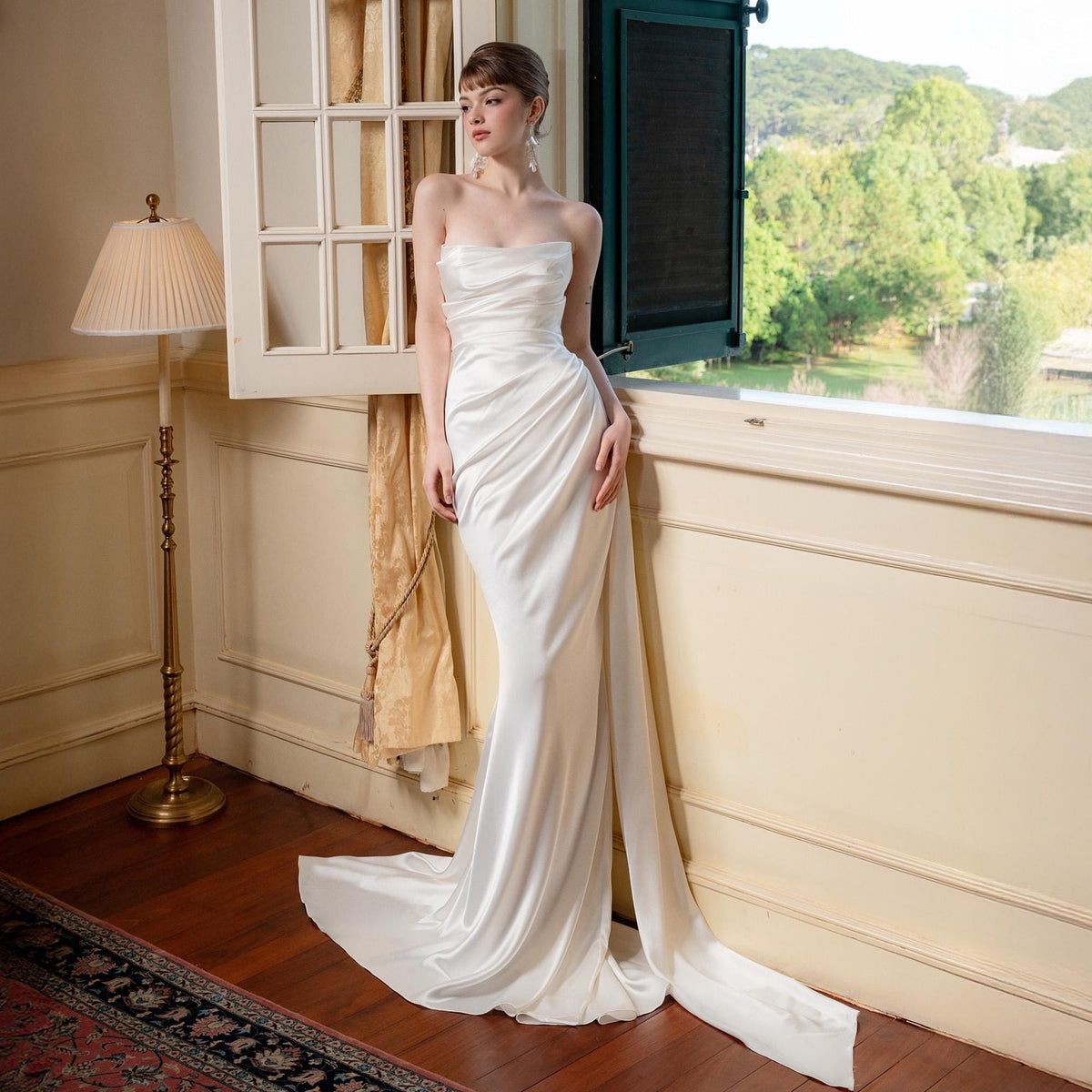 May include: A strapless, ivory-colored satin gown with a flowing train. The dress features a fitted bodice with draped detailing and a sleek, floor-length skirt. The gown is designed for a formal event.