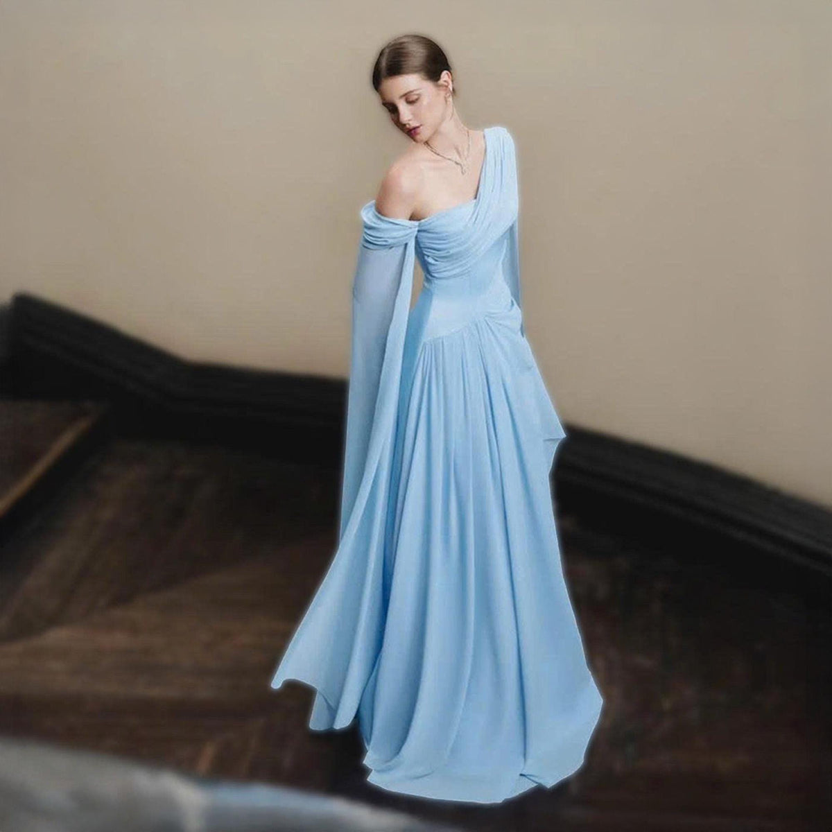 May include: A light blue, one-shoulder gown with flowing fabric. The dress features a draped bodice and long, sheer sleeves. The skirt falls to the floor, creating a graceful silhouette. The dress is suitable for formal events.