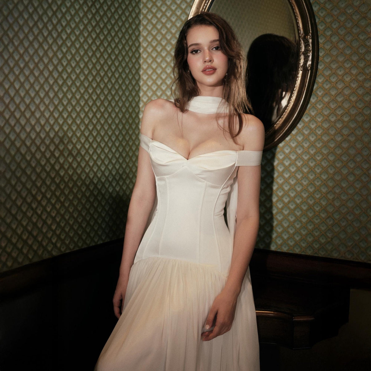 May include: A white off-the-shoulder dress featuring a structured corset-style bodice with a sweetheart neckline and a flowing, layered skirt. The garment includes a matching sheer neck scarf detail and is crafted from smooth, opaque fabric.