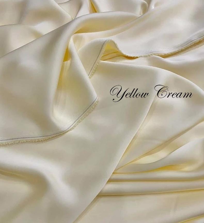 May include: A close-up of a fabric with a soft, flowing texture in a pale yellow cream color. The fabric is draped in gentle folds, with the text "Yellow Cream" in an elegant script.