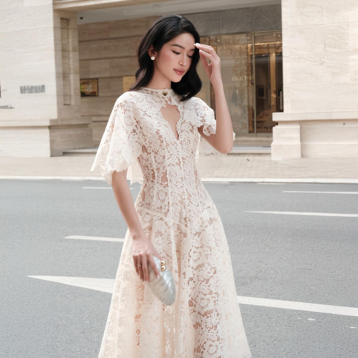 May include: A cream-colored lace midi dress featuring a high neckline with a teardrop cutout, short flutter sleeves, and a fitted bodice that transitions into a flared skirt. The intricate floral lace pattern covers the entire garment.
