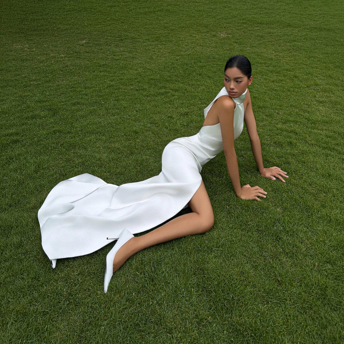 May include: A floor-length white sleeveless gown featuring a high neckline, a fitted bodice, and a dramatic side slit that extends from the thigh to the hem. The garment is paired with matching white pointed-toe high-heeled pumps.