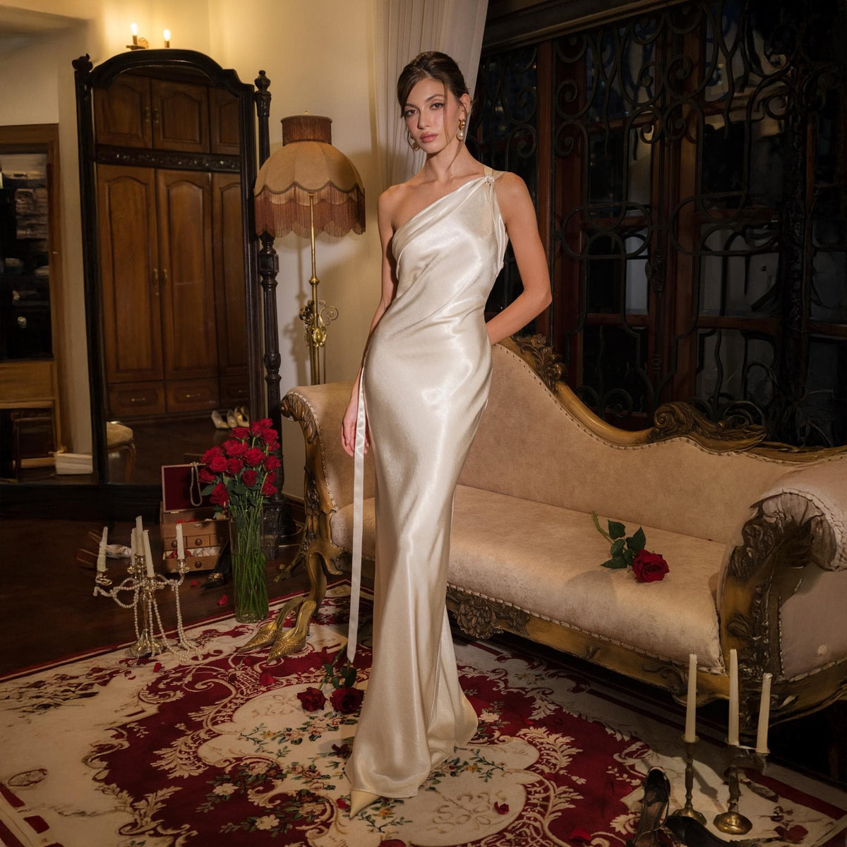 May include: A floor-length, one-shoulder cream-colored satin gown with a smooth, lustrous finish. The dress features a fitted bodice that flows into a straight, floor-length skirt, creating a sleek, elegant silhouette with a single shoulder strap.