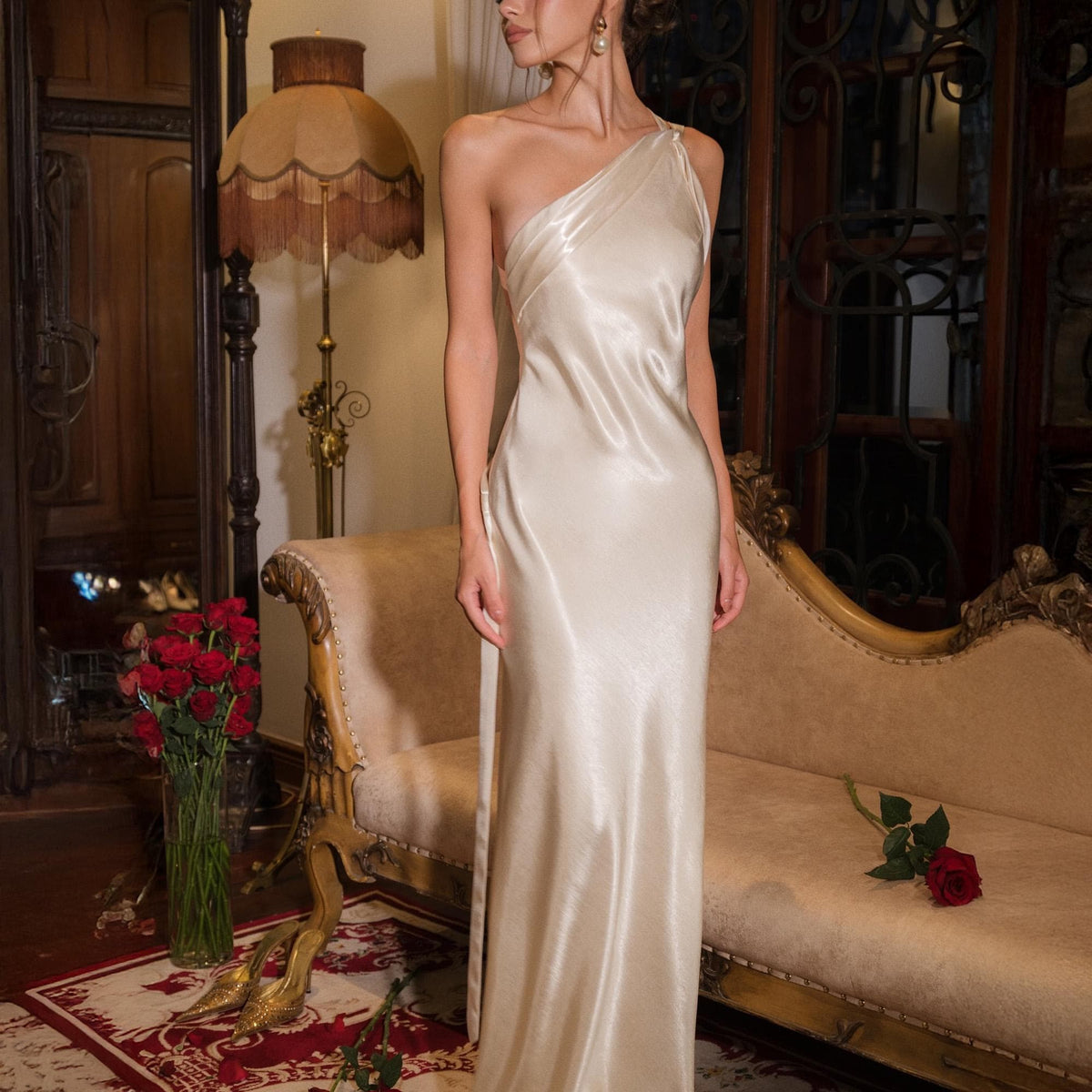 May include: A floor-length, one-shoulder gown in a lustrous, champagne-colored satin fabric. The dress features a sleek, form-fitting silhouette that drapes naturally, with a single shoulder strap and a smooth, reflective finish throughout the garment.