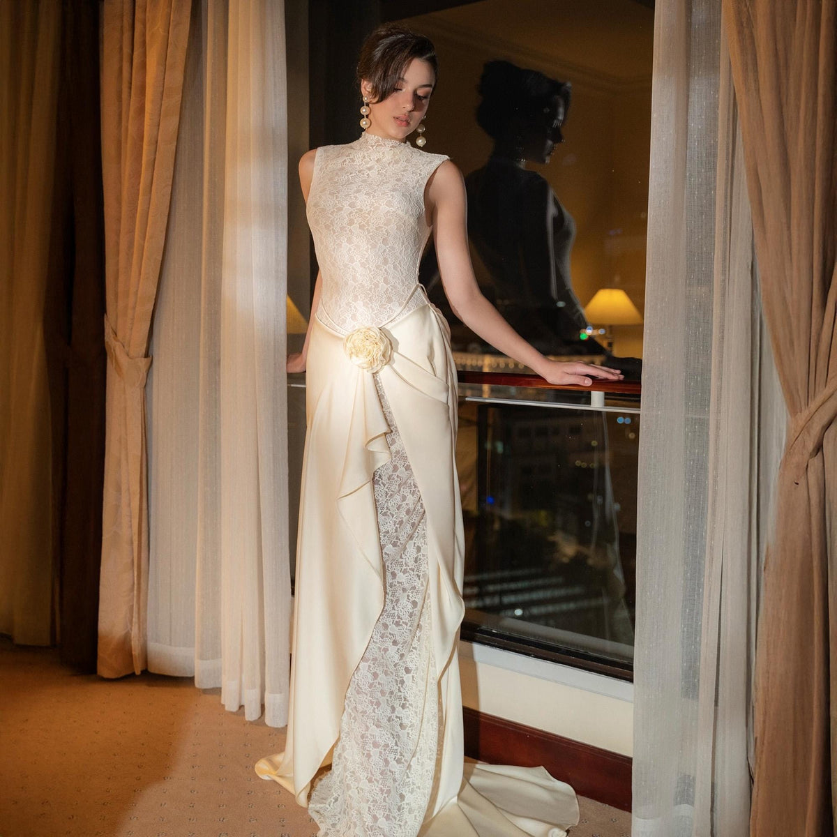 May include: A sleeveless ivory wedding gown with a high neckline and a floral accent at the waist. The dress features a lace bodice and a flowing skirt with a lace panel. The gown is floor-length and has a train.