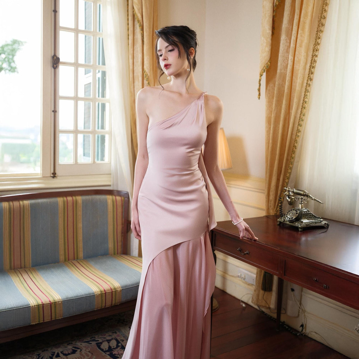 May include: A pale pink, one-shoulder formal gown. The dress features a draped bodice and a flowing skirt with an asymmetrical hemline. The fabric appears to be a smooth satin or silk. The gown is suitable for a special occasion.