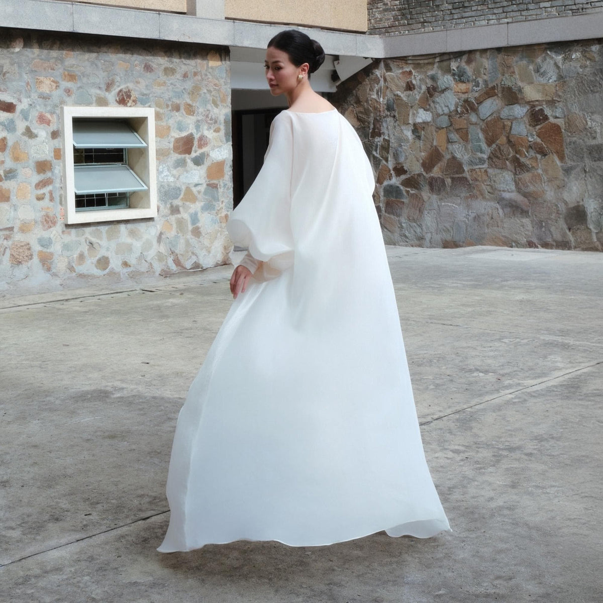 May include: A flowing, white dress with long, voluminous sleeves. The dress has a simple neckline and a full skirt, creating an elegant silhouette. The fabric appears lightweight and sheer, suggesting a formal or special occasion garment.