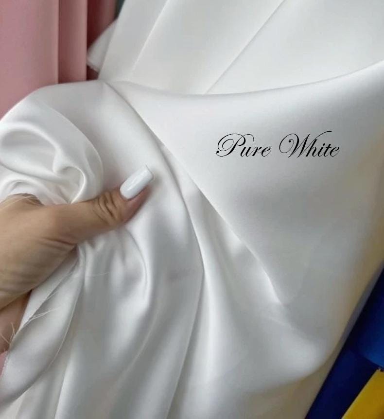 May include: A close-up of a white fabric with the text "Pure White" in a cursive font. The fabric is smooth and appears to be silk or satin. The fabric is being held by a hand with white nail polish.