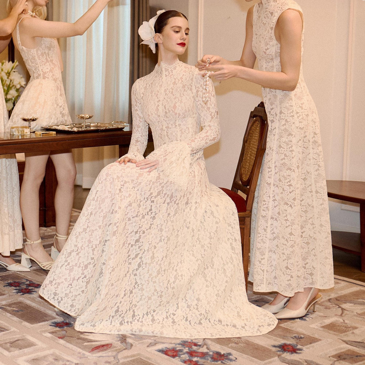 May include: A floor-length, long-sleeved cream lace dress with a high neckline and a flared skirt. The garment features an intricate floral lace pattern throughout, a fitted bodice, and a white floral hair accessory worn by the individual.