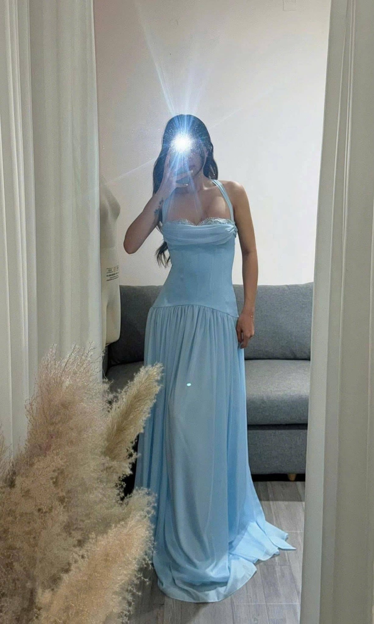 May include: A floor-length light blue gown featuring a fitted bodice with a draped neckline, a halter-style strap, and a gathered waistline that transitions into a flowing, floor-length skirt with a soft, lightweight fabric texture.