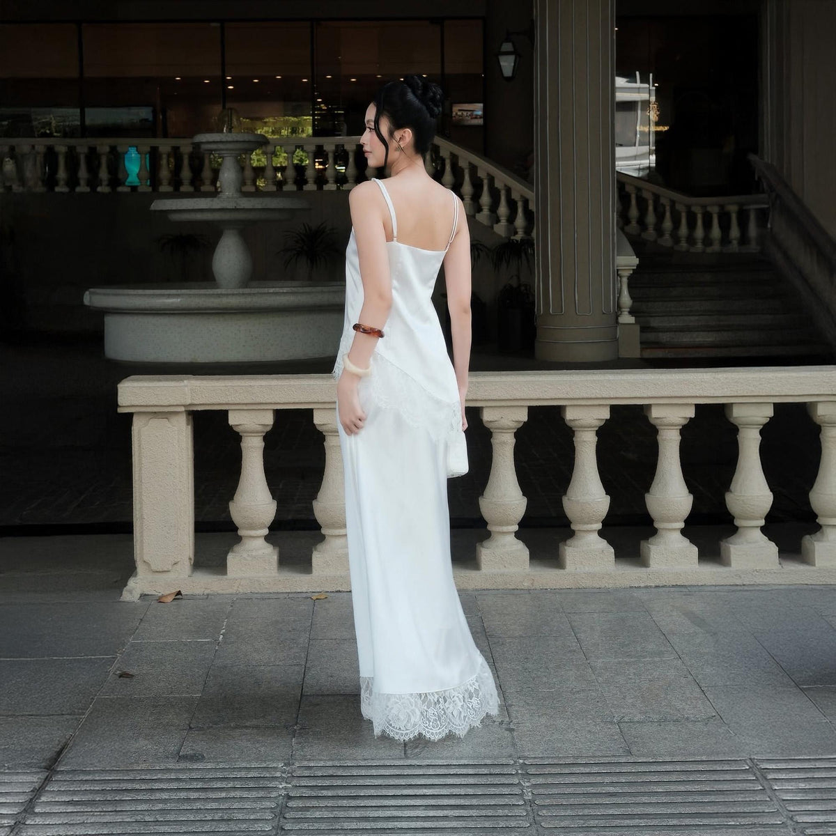 May include: A floor-length white slip dress featuring thin spaghetti straps and a delicate lace trim along the hemline. The garment is crafted from a smooth, satin-like fabric that drapes down the body, ending in a scalloped lace edge detail.