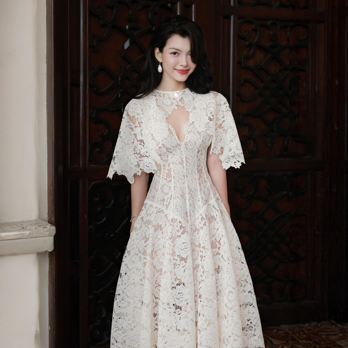 May include: A white lace midi dress featuring a high neckline with a teardrop-shaped cutout, short flared sleeves, and a fitted bodice that transitions into a full, flowing skirt. The intricate floral lace pattern overlays a solid white lining.