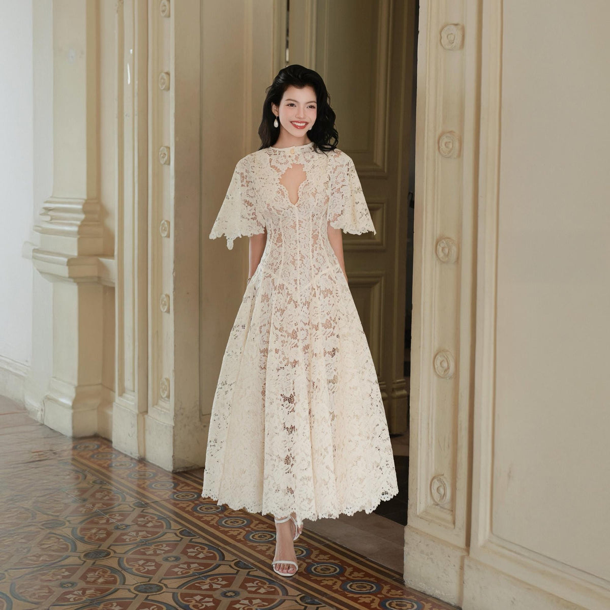 May include: A cream-colored midi-length dress crafted from intricate floral lace. The garment features short, flared sleeves, a high neckline with a central cutout, and a fitted bodice that transitions into a full, flowing skirt with a scalloped hem.