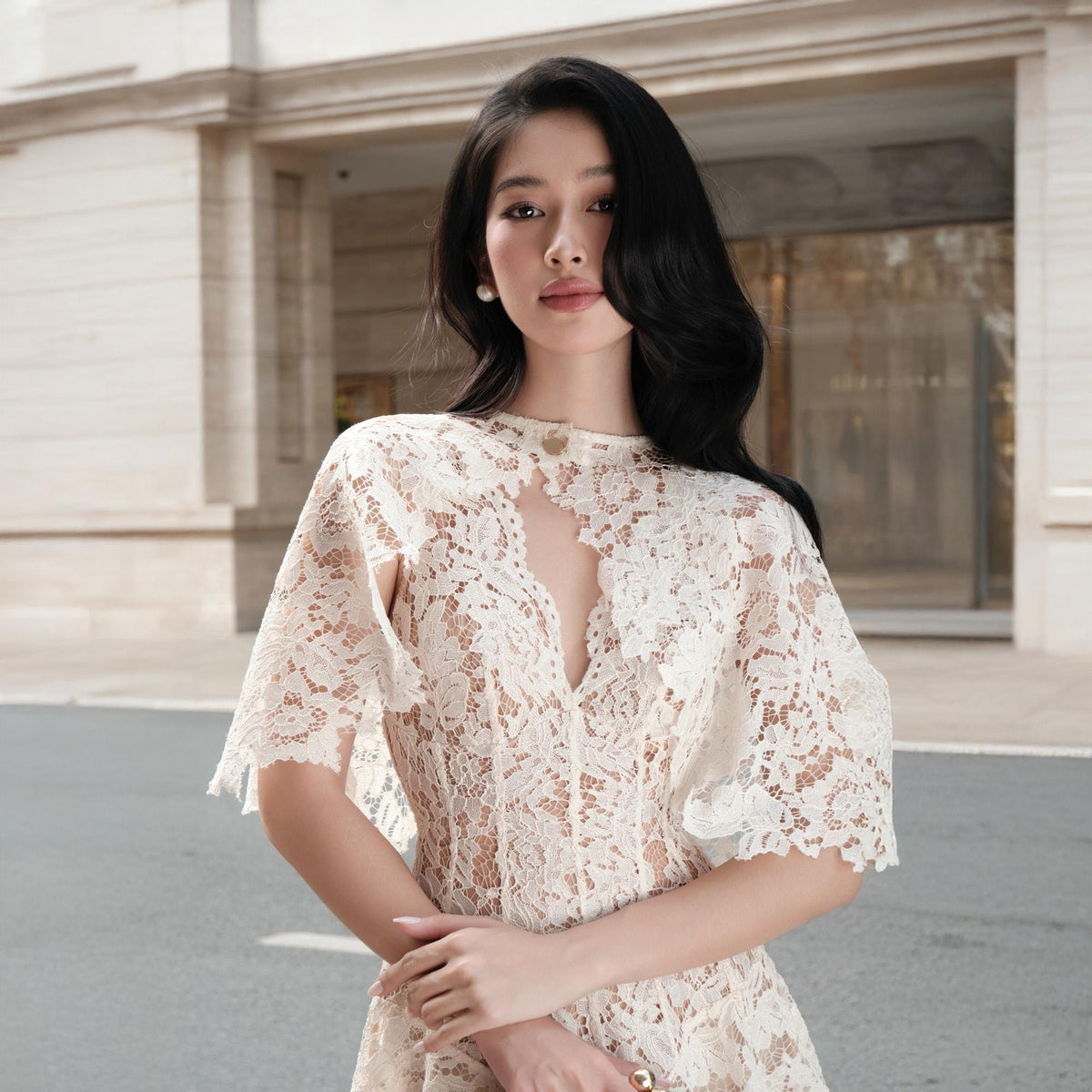 May include: A cream-colored lace dress featuring a high neckline with a central cutout, short cape-style sleeves, and intricate floral patterns throughout the fabric. The garment is constructed from delicate, semi-sheer lace material.