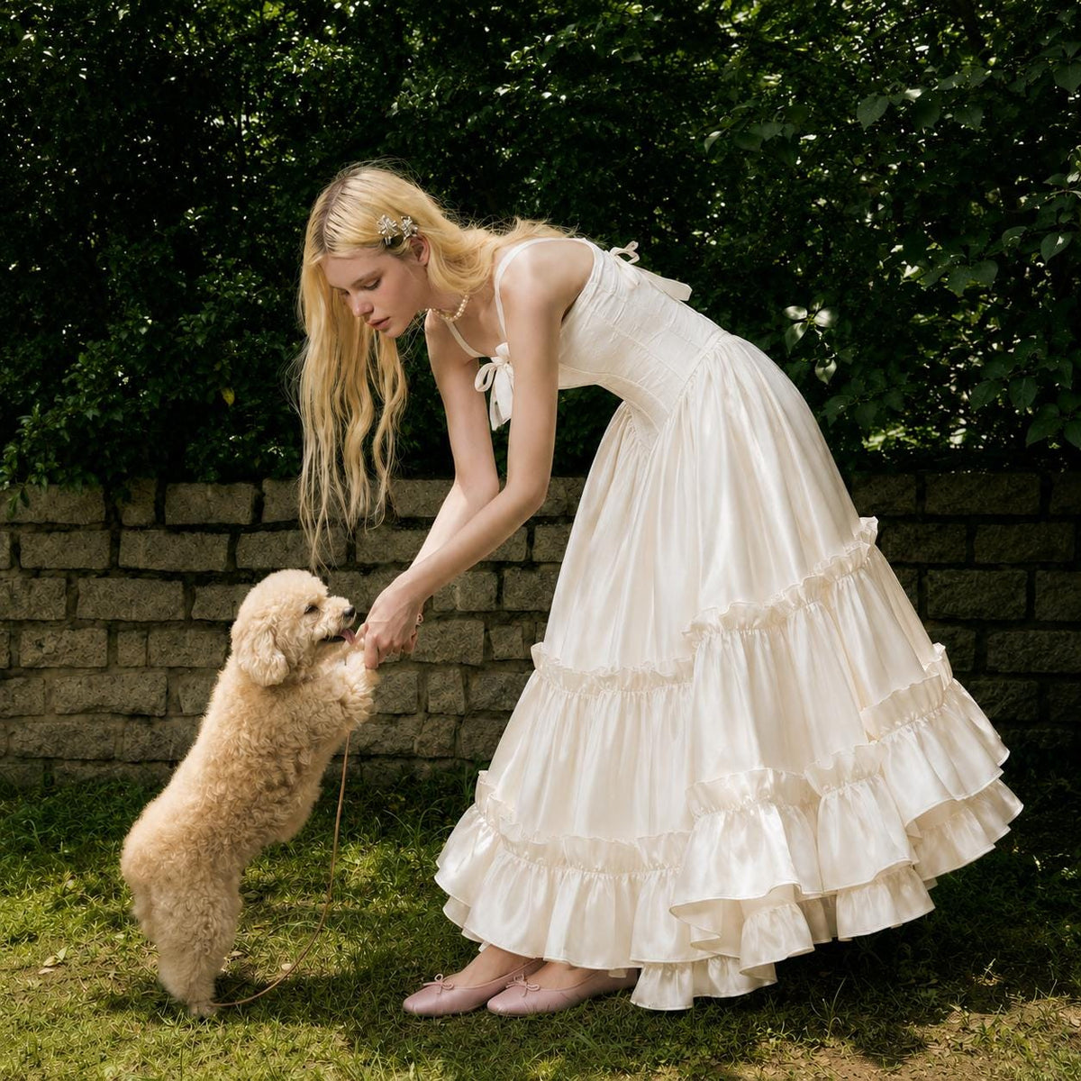 May include: A floor-length cream-colored dress with a fitted bodice, thin shoulder straps, and a multi-tiered ruffled skirt. The dress features a side-tie detail at the waist and is paired with light pink ballet flats with small bows.