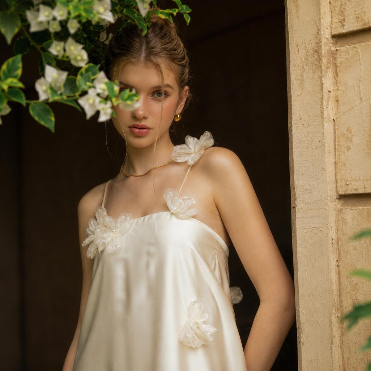 May include: A cream-colored satin slip dress featuring thin spaghetti straps and delicate, sheer floral appliqu&eacute;s attached to the straps and the bodice. The dress has a smooth, lustrous finish and a simple, straight-cut neckline design.