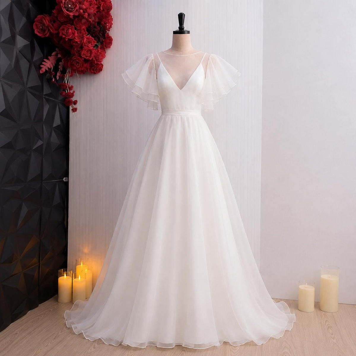 May include: A floor-length white gown featuring a sheer illusion neckline, a V-neck bodice, and flowing flutter sleeves. The dress has a fitted waistline that transitions into a full, layered skirt made of lightweight, semi-sheer fabric.