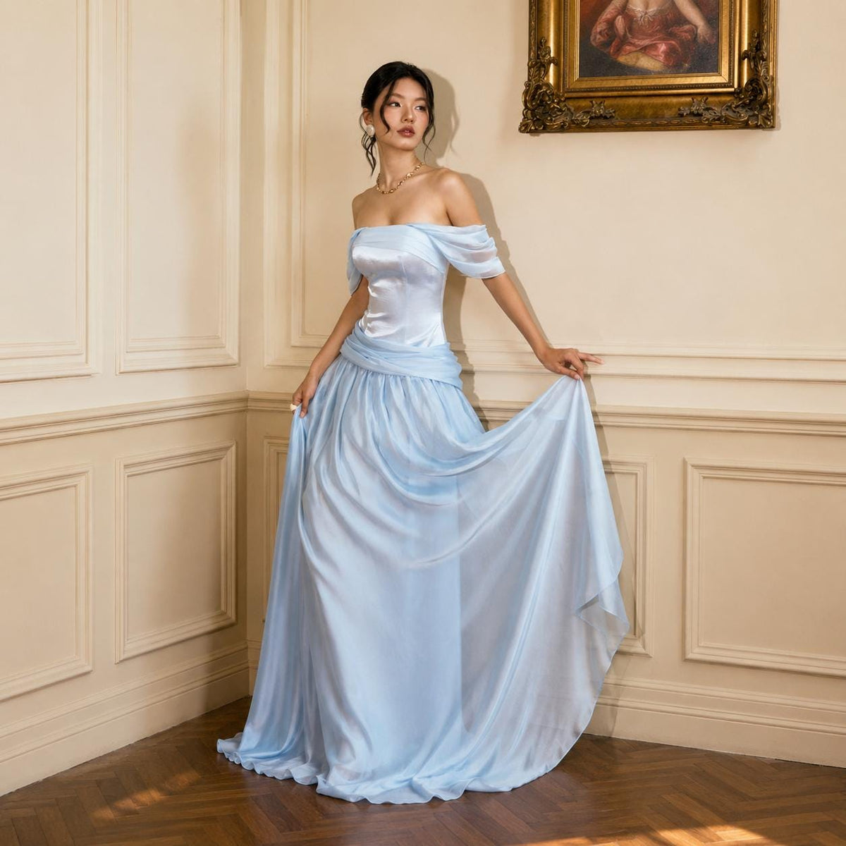 May include: A floor-length light blue gown featuring an off-the-shoulder neckline with draped short sleeves, a fitted bodice, and a flowing skirt with a gathered waistline detail. The dress is made of a smooth, satin-like fabric with a soft sheen.