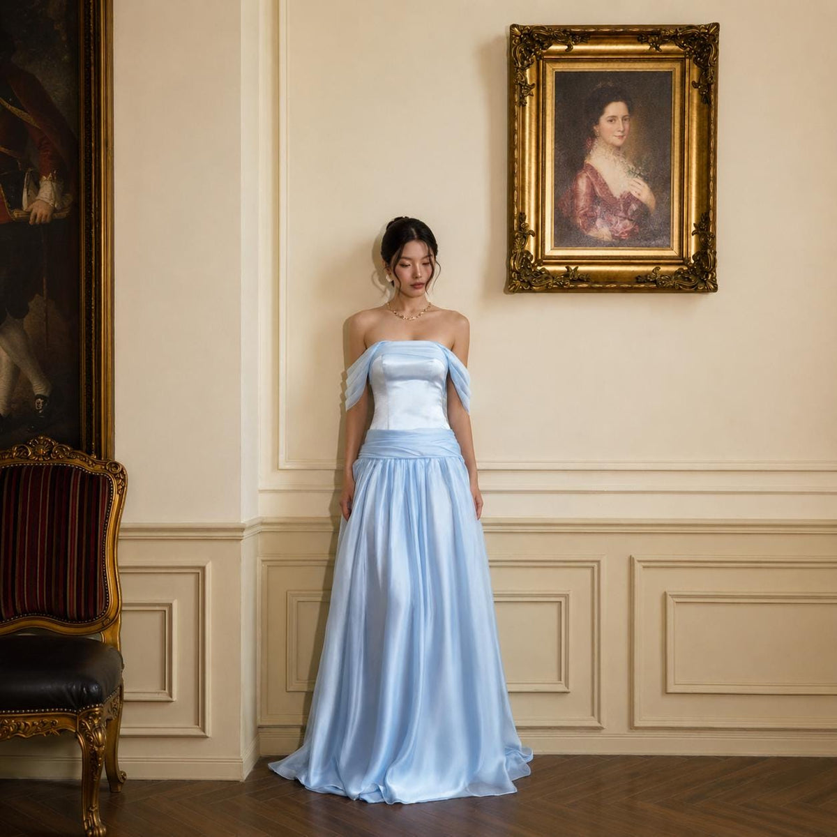 May include: A floor-length, light blue satin gown featuring an off-the-shoulder neckline with draped sleeves, a fitted bodice, and a flowing, floor-length skirt. The dress is made of a smooth, lustrous fabric that catches the light.