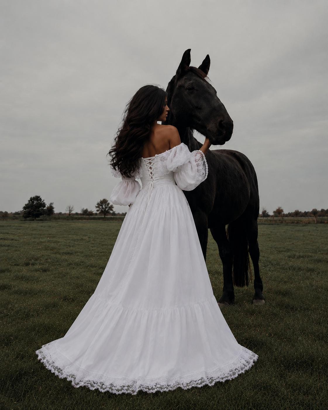 May include: A floor-length white dress with off-the-shoulder puff sleeves, a lace-up corset back, and a tiered skirt with a lace hem. The garment is shown next to a large black horse in an open field under a cloudy, overcast gray sky.